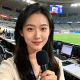 一位25岁左右的中国女性体育记者半身照，手持录音笔，背景为体育场媒体工作区
